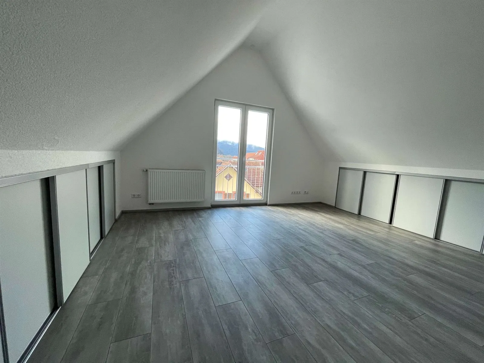 Dachgeschoss mit grauem Boden, Balkontür und verkleideten Dachschrägen